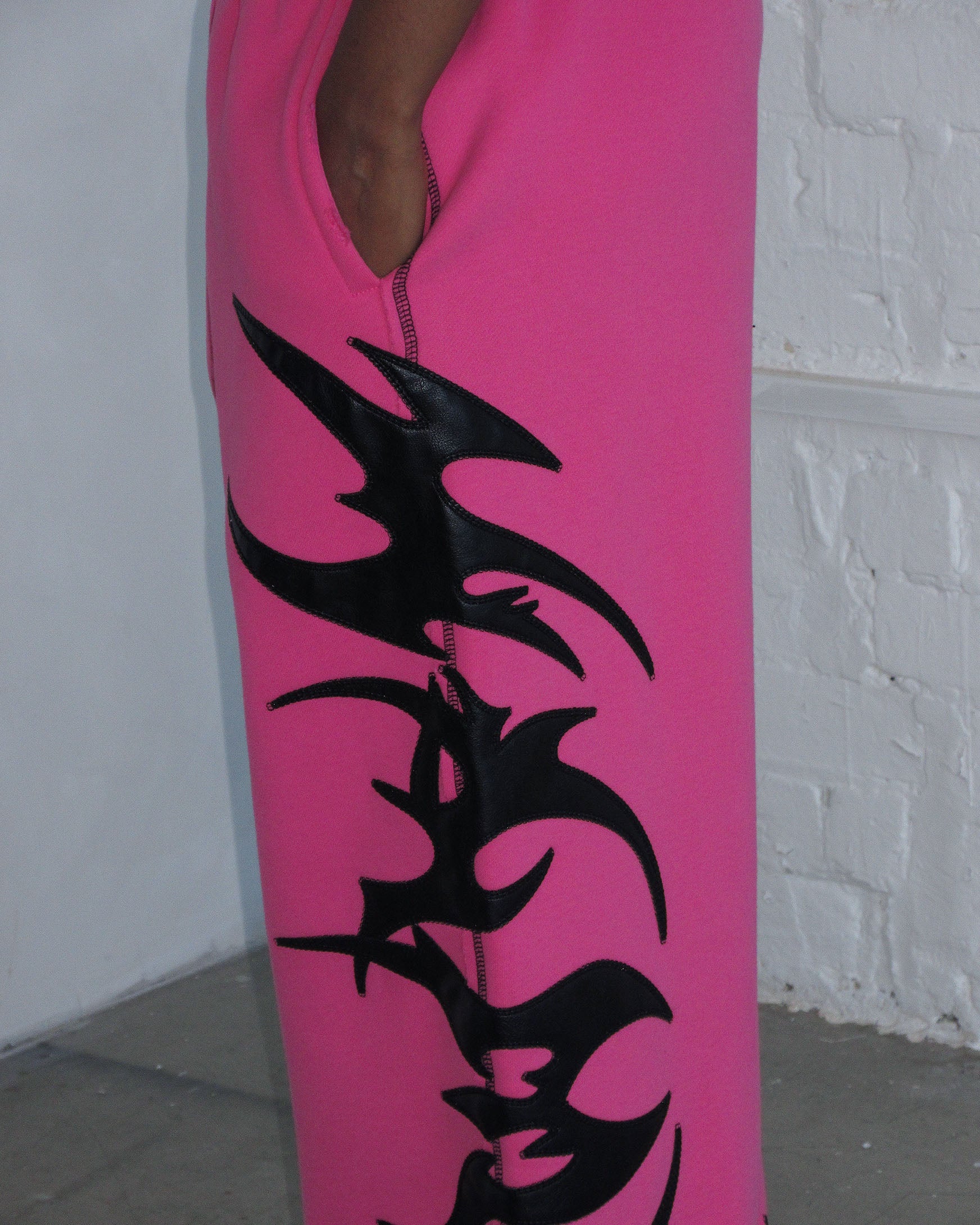 Person wearing NAMED collective FLAME SWEATPANTS PINK POISON, standing by a white brick wall.