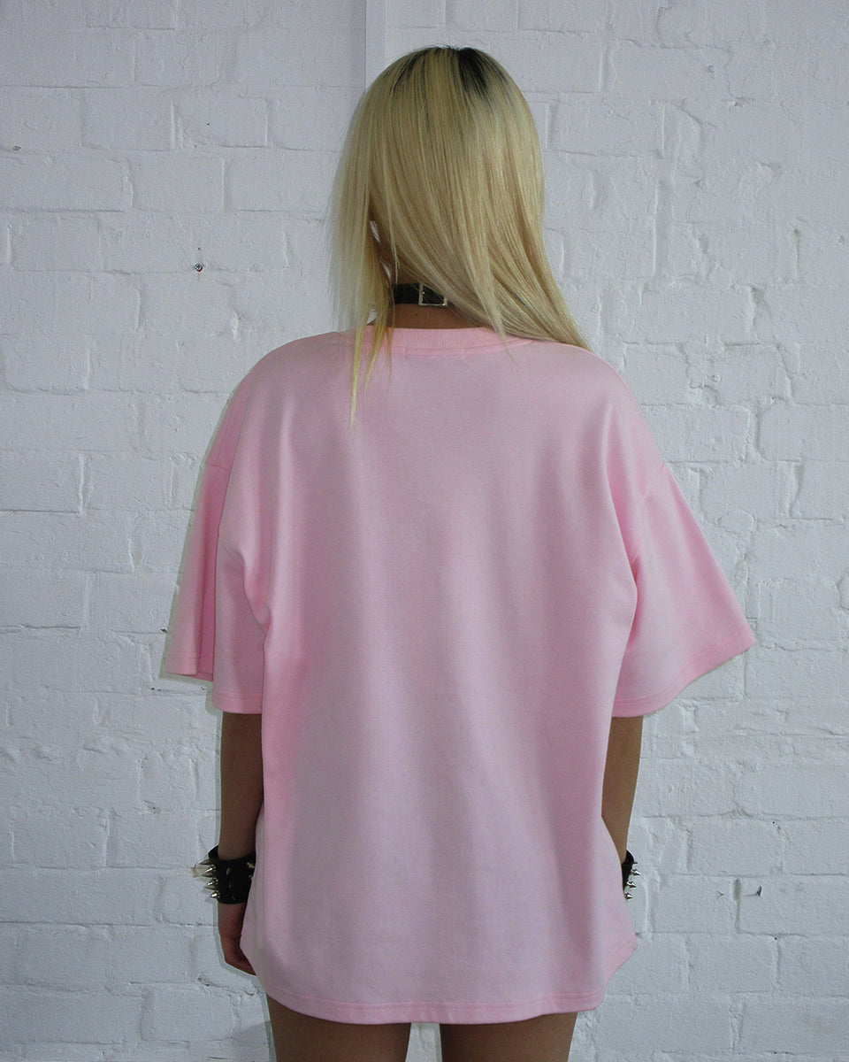 Person with straight blonde hair wears the NAMED COLLECTIVE® 404 ERROR KITTY OVERSIZED TEE BABY PINK, back to camera.