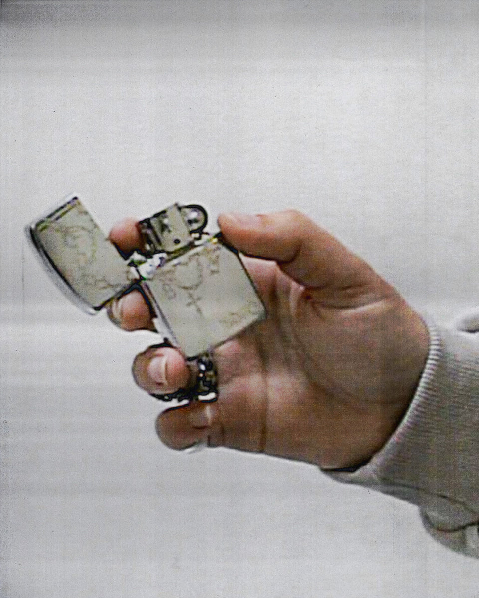 A hand holds a NAMED COLLECTIVE® CHAINS REFILLABLE LIGHTER with its metal flip-top lid open against a plain background.