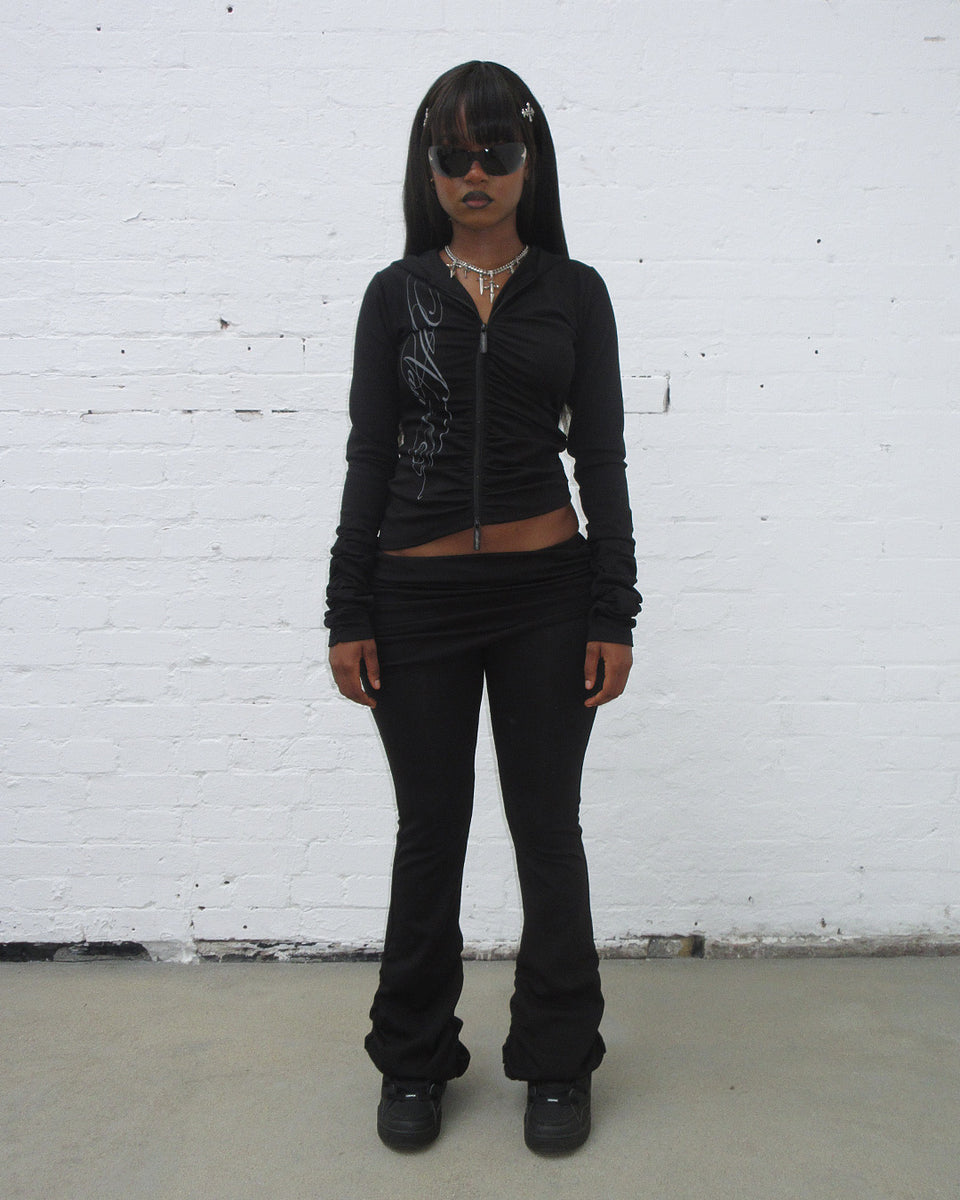 Model wearing Crush sculpt stretch drape pants black with matching black sweatpants and black sunglasses.