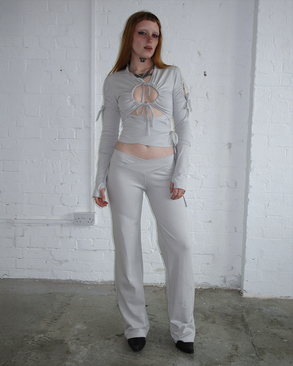 Model wears the ENVY SCULPT STRETCH TIE HOODIE in Mist Grey by NAMED COLLECTIVE® against a white brick wall.