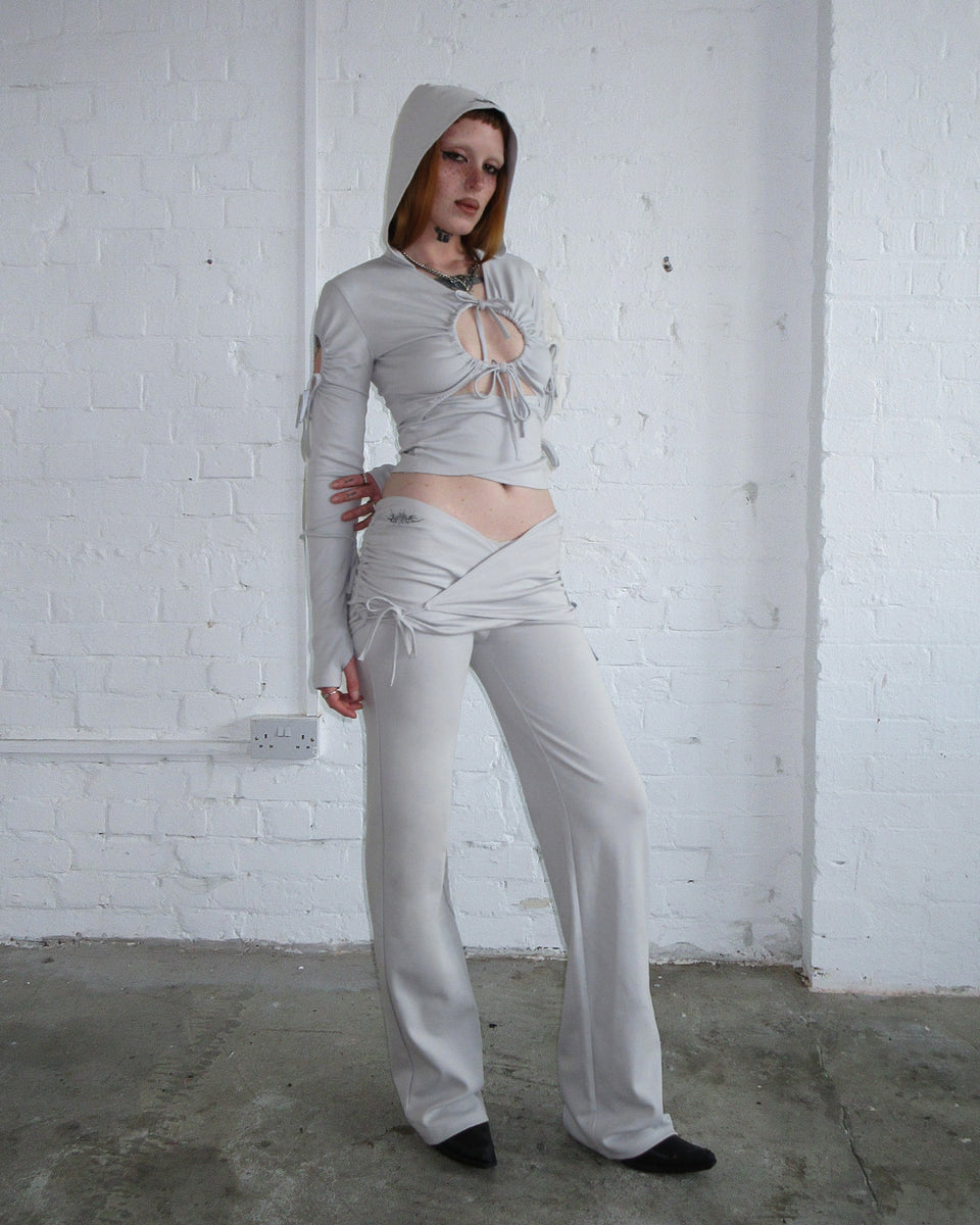 Person wears the ENVY SCULPT Stretch Two Piece Skirt Trouser Set in Mist Grey by NAMED COLLECTIVE® against a white wall.