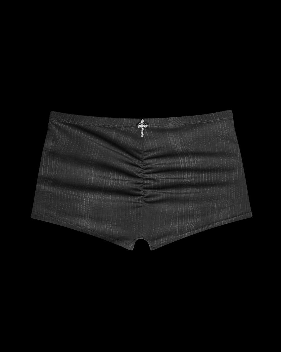 NAMED COLLECTIVE® ENVY Snakeskin Hotpant Shorts in charcoal with a center cross charm, shown on a black background.