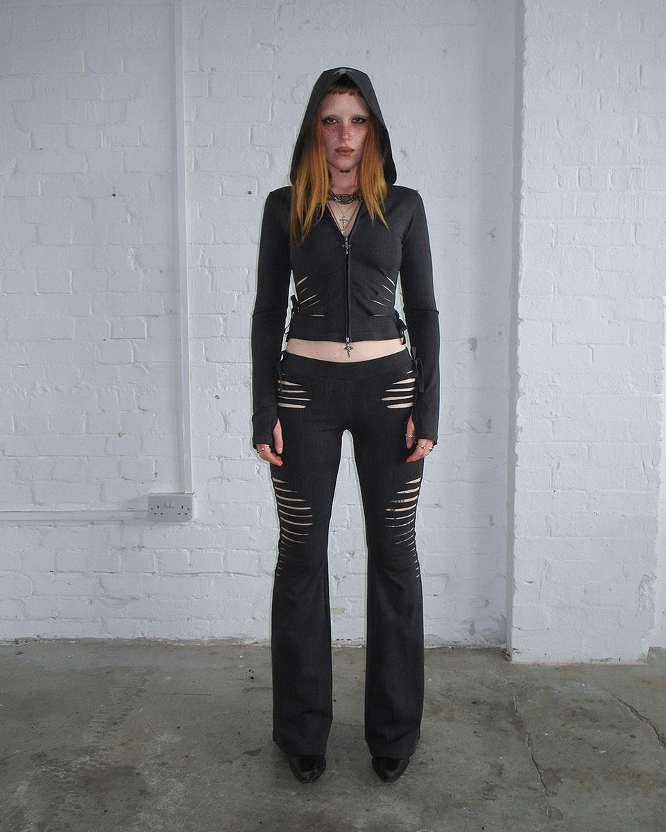 Person stands against white brick wall in NAMED COLLECTIVE® ENVY SNAKESKIN SLASHED SCULPT STRETCH PANTS CHARCOAL.