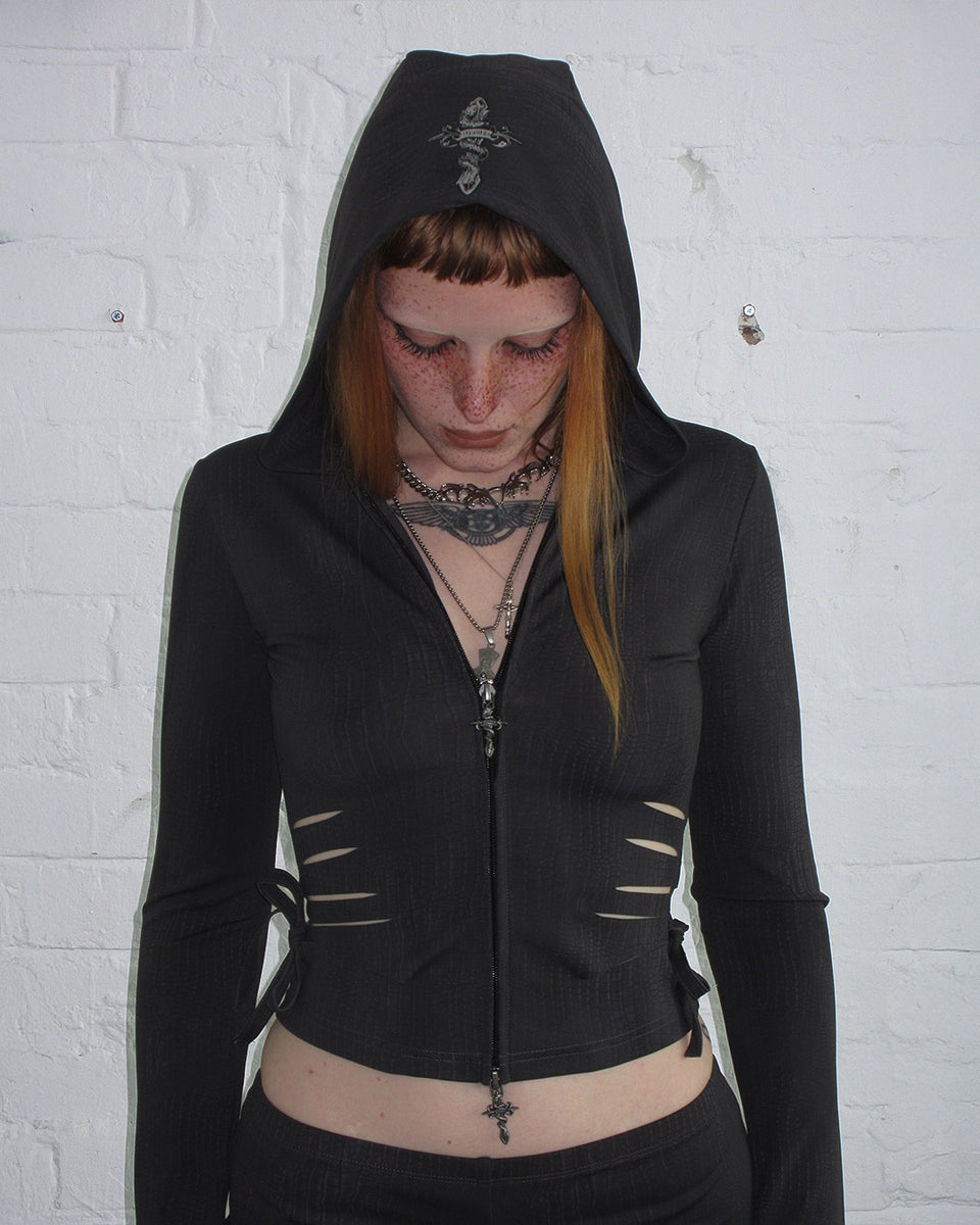 Person with straight red hair and bangs wears NAMED COLLECTIVE® ENVY SNAKESKIN SLASHED HOODIE in charcoal.