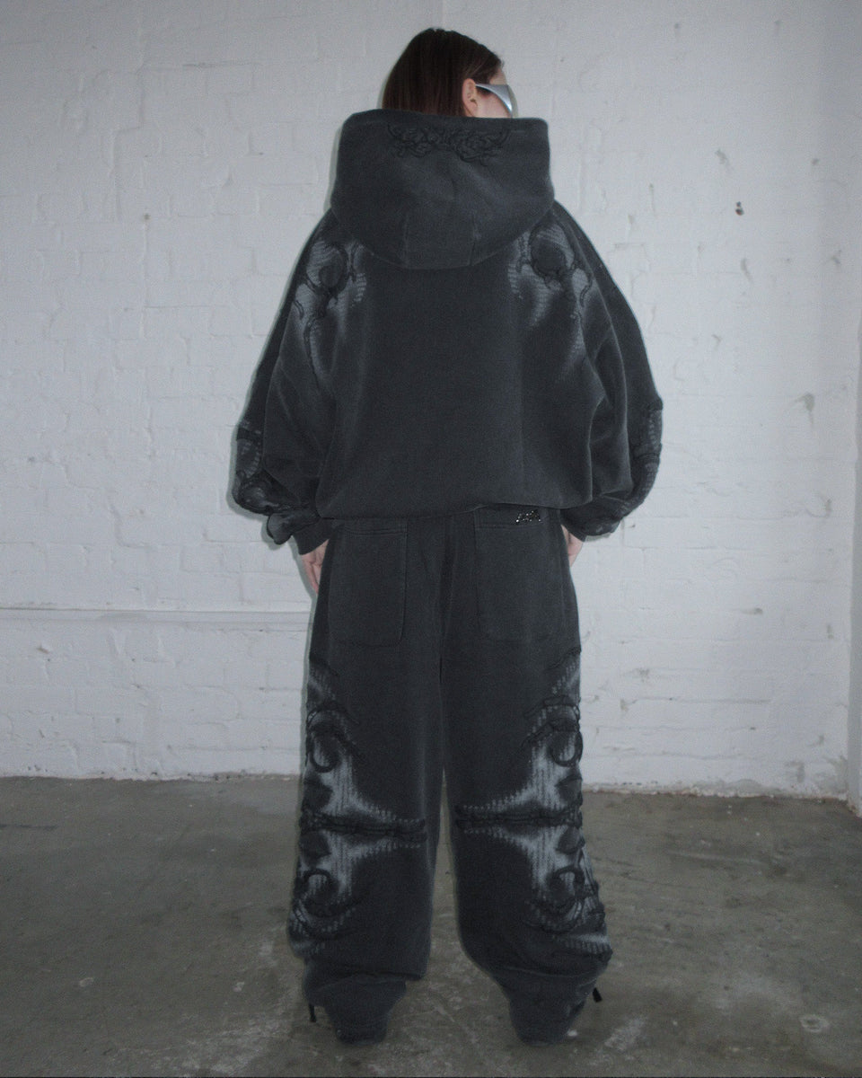Person wears NAMED COLLECTIVE® EUPHORIA PUFF PRINT oversized sweatpants in washed charcoal by a white brick wall.