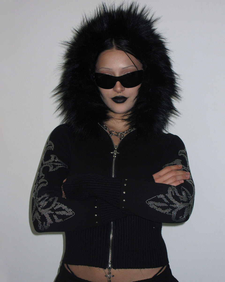 Person in NAMED COLLECTIVE® FERAL FAUX FUR FITTED ZIP HOODIE BLACK with detachable fur stands arms crossed, sunglasses on.