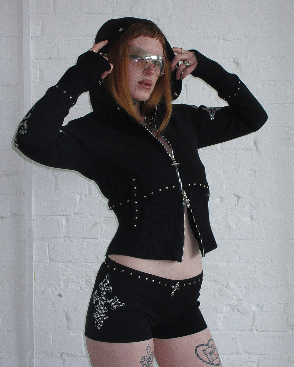 Person wears NAMED COLLECTIVE® FERAL Faux Fur Fitted Zip Hoodie in black, posing by a white brick wall.