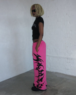 Person standing sideways in a room, wearing NAMED collective FLAME SWEATPANTS PINK POISON and a black t-shirt.
