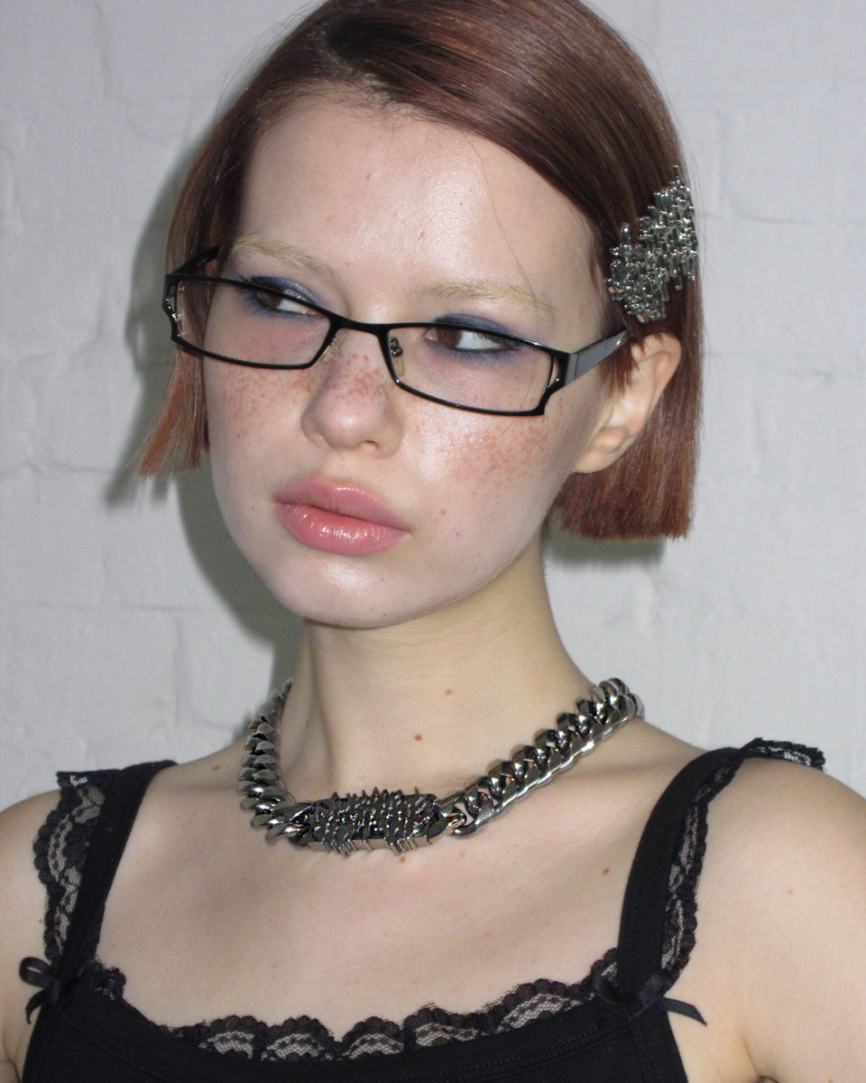 Young person with short hair, glasses, black top, decorative hair clip, wears NAMED COLLECTIVE® GHOST LOGO CHAIN 18MM.