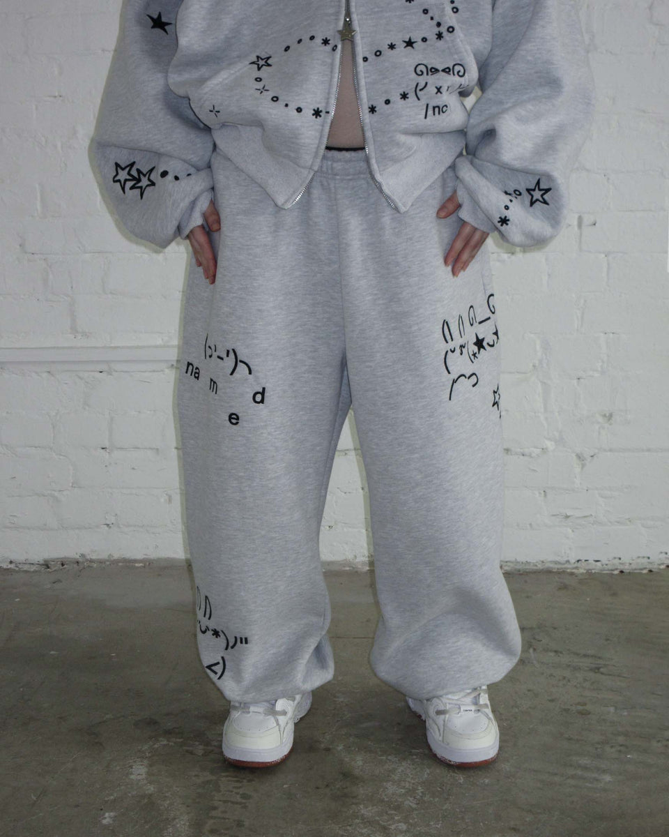 Model wears NAMED COLLECTIVE® MALFUNCTION SWEATPANTS GREY MARL with matching sweatshirt, standing by a white brick wall.