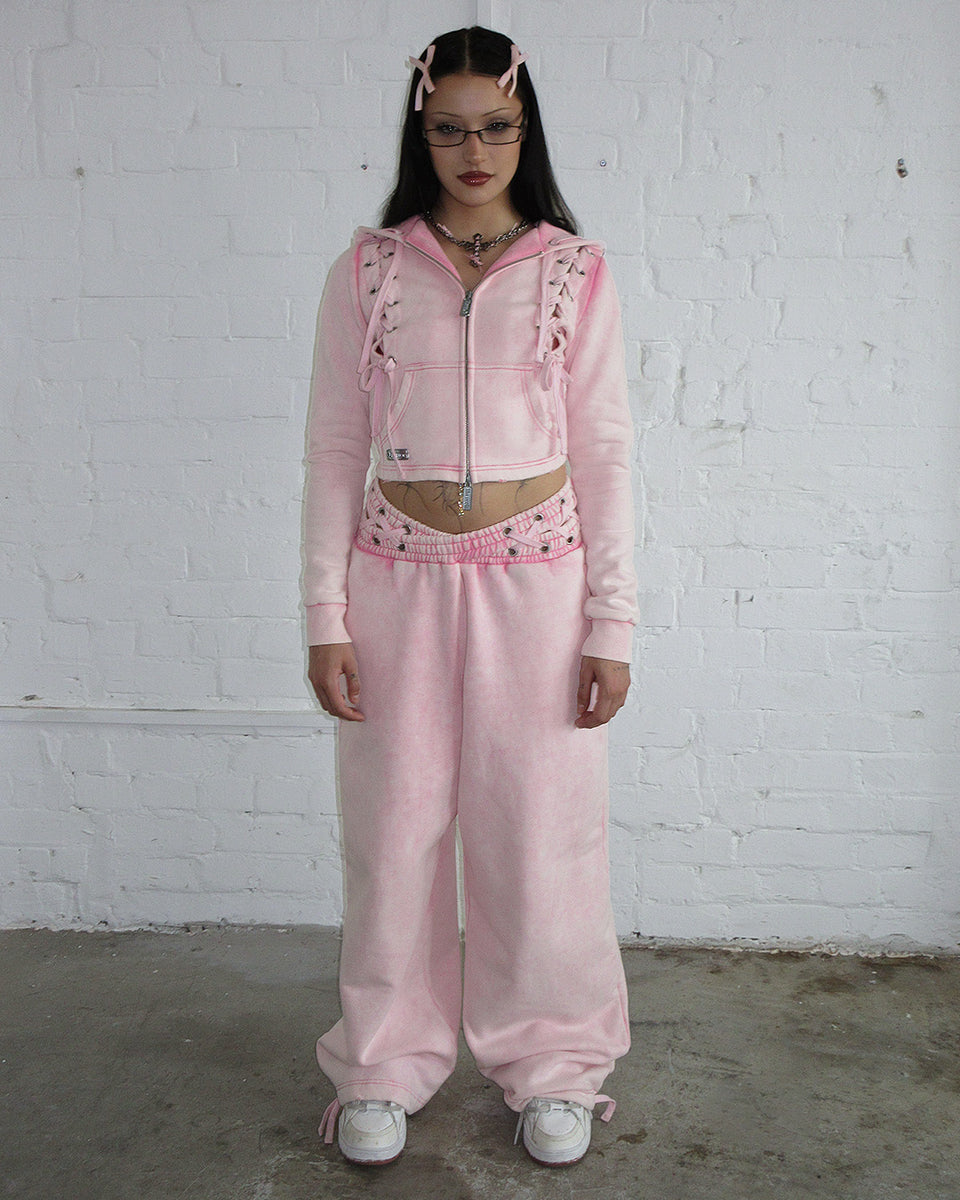 Model wearing Vendetta oversized sweatpants in washed baby pink with cross-over waistband, made from organic cotton and recycled fleece.