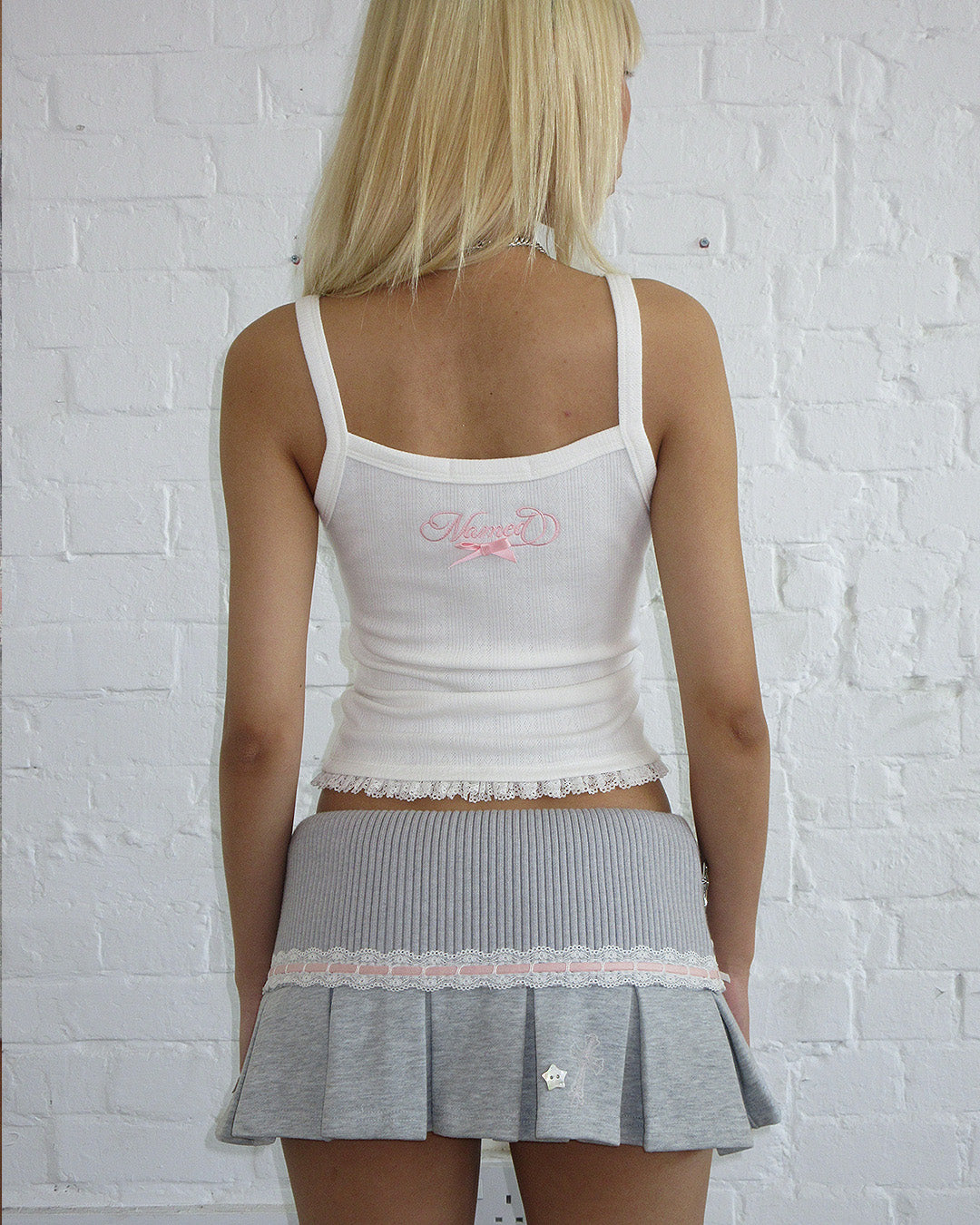 Person with long blonde hair wears NAMED COLLECTIVE® WHISPER PLEATED MINI SKIRT GREY MARL and a white tank top.