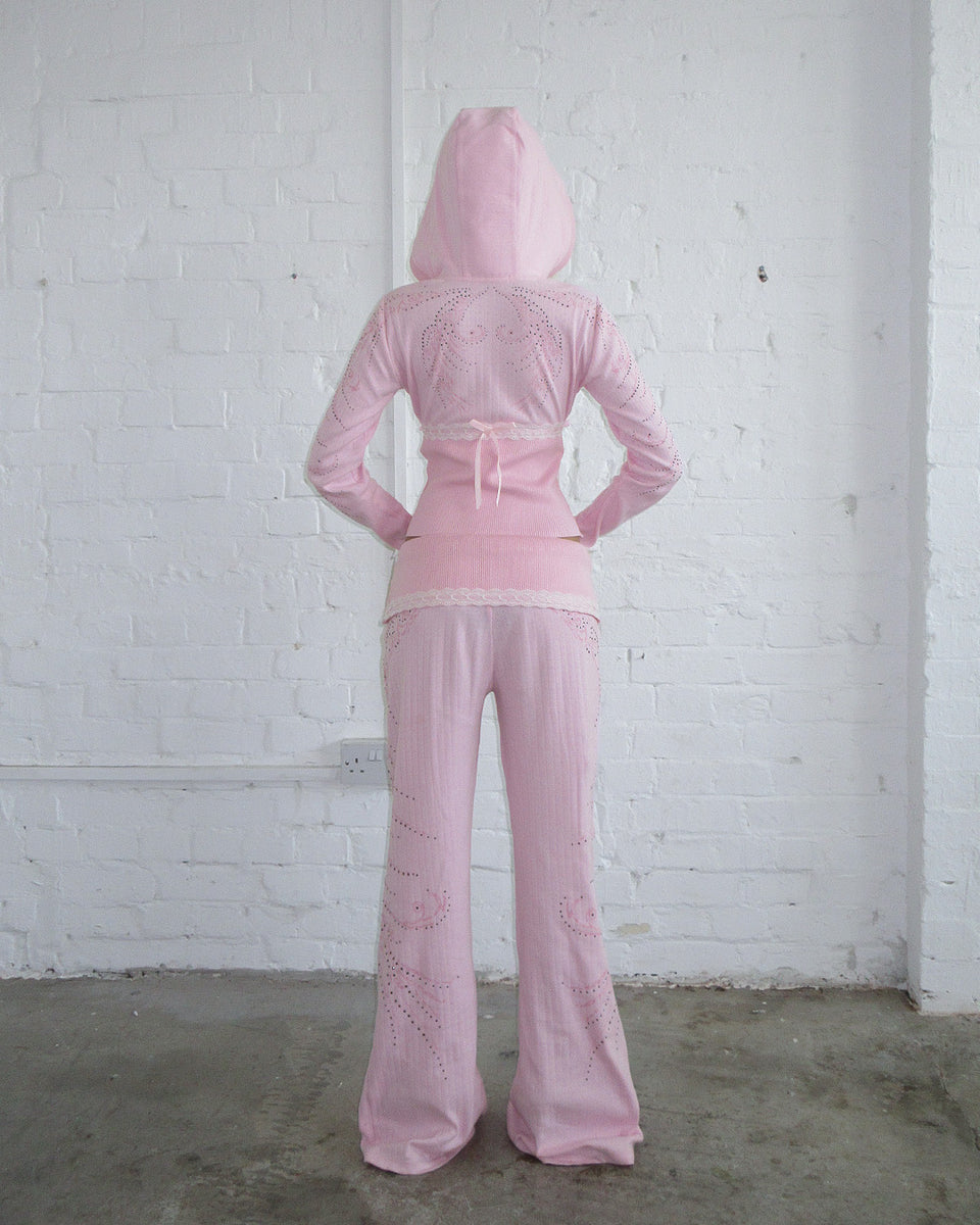 Model wears NAMED COLLECTIVE® WHISPER RIBBON POINTELLE SCULPT PANTS in baby pink, facing a white brick wall.