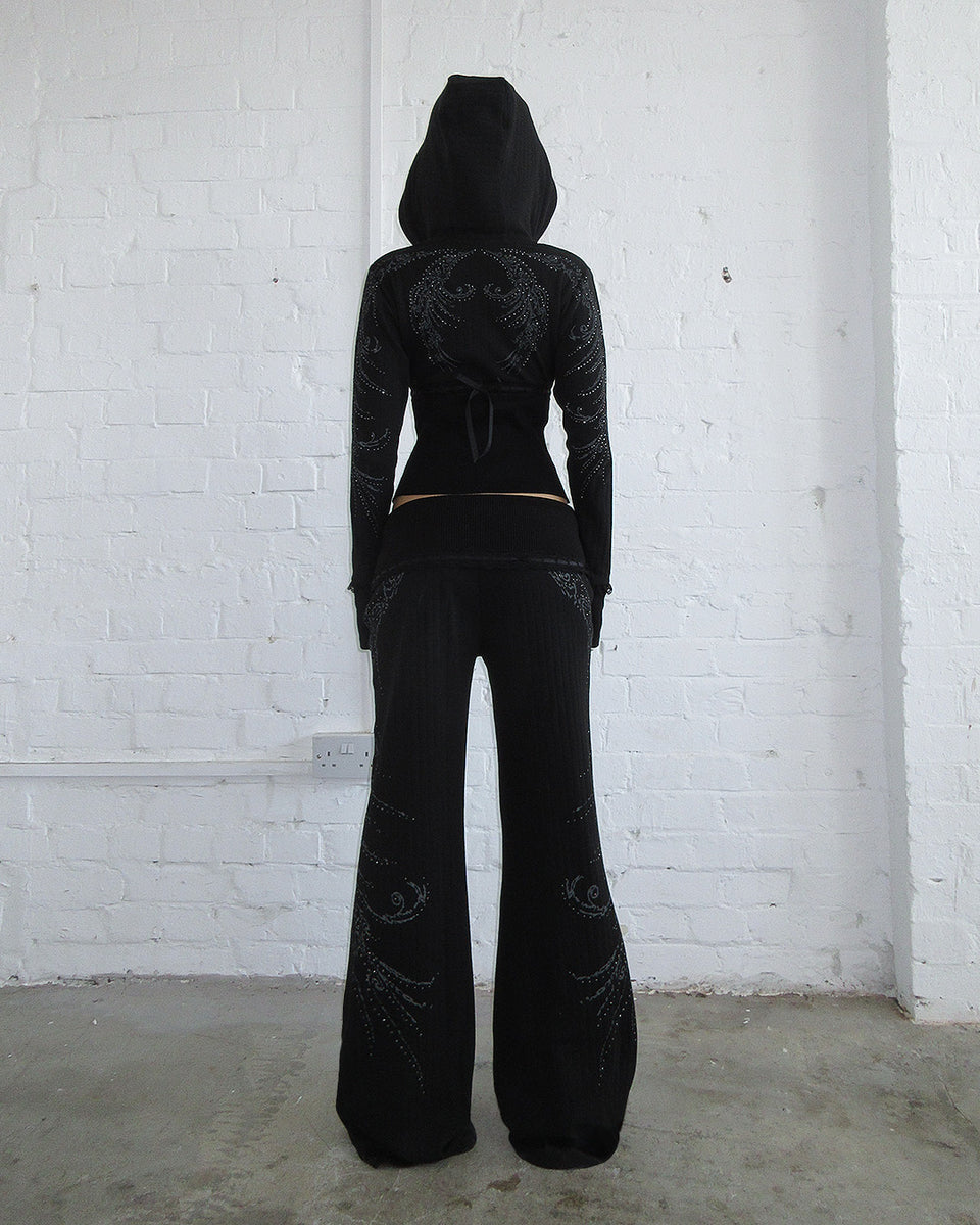 Person faces away in black NAMED COLLECTIVE® WHISPER RIBBON POINTELLE SCULPT PANTS against a white brick wall.